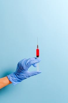 A gloved hand holds a syringe with red liquid, set against a blue background.
